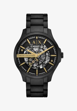 Reloj automático negro con un dial transparente, acentos dorados, grandes números en negrita y una pulsera de eslabones de metal. Mecanismos internos con un patrón visibles.