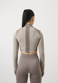 Langermet, cropped treningsgenser i lys beige med ribbestruktur og ventileringsdetaljer bak. Kombinert med matchende, teksturerte høytlivsleggings.