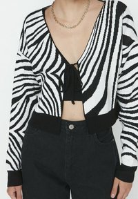 Svart och vit randig kort cardigan med djup V-ringning, knyt fram stängning och ribbade ärmar, kombinerad med högmidjade svarta jeans.