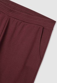 Bordowe dresy wykonane z miękkiego materiału, z elastycznym paskiem w talii i bocznymi kieszeniami dla większej funkcjonalności. Gładka tekstura na całej powierzchni.