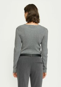 Grau gestreifter Pullover mit langen Ärmeln und rundem Ausschnitt, kombiniert mit grauen strukturierten Hose und einem schwarzen glänzenden Gürtel.
