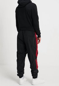 Zwarte hoodie met een comfortabele pasvorm. Zwarte joggers met rode strepen aan de zijkant en elastische boorden. Witte sneakers maken de outfit compleet.