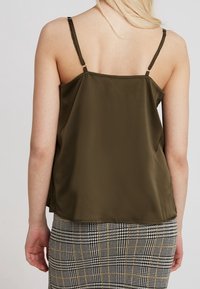 Oljen grøn satin camisole med tynne justerbare stropper, glatt tekstur og avslappet passform, sammen med et rutete mønster skjørt.