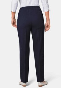 Marineblauwe broeken met een rechte pijpdesign, voorzien van een elastische tailleband en subtiele streepjes, gecombineerd met lichtgekleurde platte schoenen.