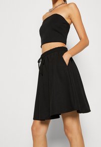 Svart kort topp med en slät yta och en figurnära stil, sammanvävt med en svart A-linje kjol med elastisk midja och sidofickor.