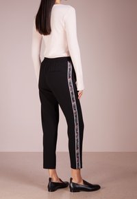 Zwarte tappered broek met een gestructureerde bloemenzijkant en een elastische tailleband, gecombineerd met een lichtroze aansluitende trui en zwarte flats.
