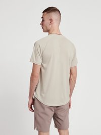 Beige kortärmad sporttröja med raglanärmar, gjord av slät tyg, har en rundad nederkant, bärs med ljusbruna shorts.