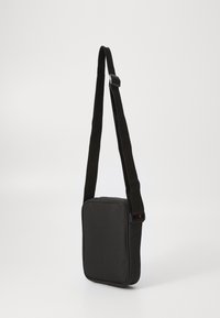 Borsa a spalla nera con forma rettangolare, realizzata in tessuto resistente. Presenta una tracolla regolabile e una chiusura con zip nella parte superiore.