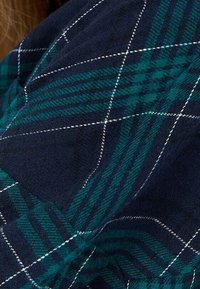 En flanellskjorta med en marinblå bas, med ett grönt och svart rutmönster, vita sömmar och mjuk textur.