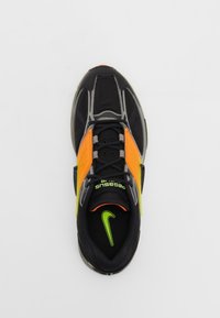 Černá teniska s oranžovými akcenty a stříbrnými detaily. Má texturovaný svršek a výrazné zelené logo Nike na patě.