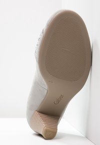 Chaussure en suède gris avec un talon de hauteur intermédiaire, dotée d'une semelle extérieure en caoutchouc texturé et du nom de la marque "Gabor" embossé au fond.