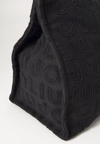 Borsa in tessuto nero con pattern logo testurizzato, caratterizzata da una forma strutturata e bordi cuciti, che mette in evidenza la sua superficie morbida e il design unico.