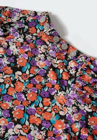 Tissu floral avec des fleurs orange, violettes, blanches et bleu sarcelle sur fond noir, orné de cinq boutons décoratifs en forme de fleur argentés sur un col froncé.