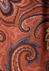 Tissu avec un motif paisley détaillé en tons rouille, marron, bleu et or, présentant des formes tourbillonnantes rappelant des feuilles et des lignes fines et délicates.