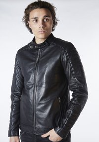 Chaqueta de cuero negro con cierre de cremallera, cuello a presión y detalles acolchados en los hombros. Textura suave con bolsillos laterales con cremallera.