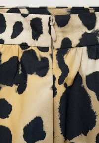 Látka s leopardím potiskem v béžové a černé barvě se skrytým zipem u pásu. Texturovaný, skladovaný design s zaoblenými tvary.