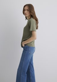 Olive green cotton t-shirt with short sleeves, paired with light blue wide-leg jeans featuring a back pocket on the right side.