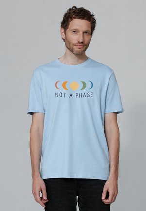Hellblaues Baumwoll-T-Shirt mit einem Grafikdesign der Mondphasen in Orange, Gelb, Grün und Blau, versehen mit dem Text "NICHT EINE PHASE" in Schwarz.