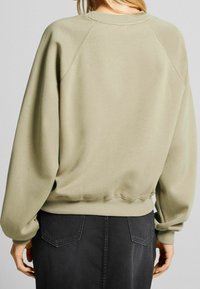 Överdimensionerad sweatshirt i salvgrön med ribbat krage och mudd. Raglanärmar och elastisk nederkant. Buren med en svart kjol med bakfickor.