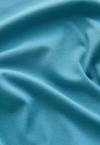 Tissu bleu clair doux avec une texture fine de maille visible et des plis délicats créant des courbes douces et fluides.