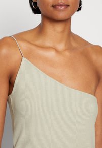 Top in tessuto a coste verde chiaro con una spallina singola e finitura testurizzata, caratterizzato da un collo asimmetrico e un design semplice.