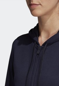 Felpa con zip di colore blu navy, dotata di cappuccio regolabile con cordini, realizzata in tessuto morbido e con cuciture visibili lungo la zip per una maggiore durata.