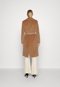 Bruin gewatteerd jasje met een gestructureerde afwerking, voorzien van een schouderkraag en een dubbel-breasted ontwerp, gedragen over witte flared broek.