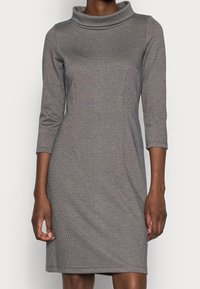 Šaty s kapucí vyrobené z texturované šedé látky s kostkovaným vzorem, úzký střih, tříčtvrteční rukávy a rovný lem.