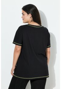 Camiseta negra de manga corta, con costuras verdes en el cuello y el dobladillo. La tela parece suave y tiene un corte relajado.