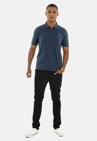 Navy polo shirt with short sleeves, featuring a collar and a small emblem. Paired with fitted black jeans and white sneakers.