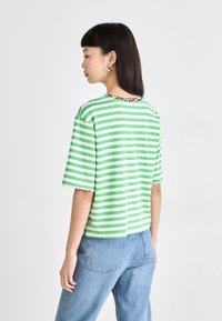 Groen met witte gestreepte t-shirt met korte mouwen en een kraag in luipaardprint, gecombineerd met blauwe jeans. Heeft een relaxte pasvorm en een zachte textuur.