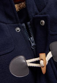 Marineblaues Wolljackett mit Reißverschluss, Lederakzenten und Holzverschluss. Fleece-Futter im Kragenbereich sichtbar.