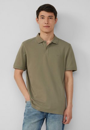 Olivgrünes Kurzarm-Polohemd mit Kragen, zwei Knöpfen und gesticktem Logo auf der Brust, kombiniert mit hellblauen Jeans.