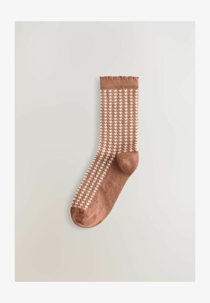 Brun sok med et hvidt houndstooth-mønster og en ribbet manchet øverst, præsenteret mod en lys baggrund.