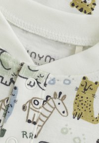 Kurzärmliger cremfarbener Body mit verschiedenen Cartoon-Tiermotiven. Weicher Baumwollstoff mit Druckknöpfen am Hals und am unteren Ende.