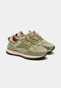 Zapatillas deportivas de color verde claro con detalles beige, que presentan una parte superior texturizada, un collar acolchado y una suela de caucho duradera, diseñadas para la comodidad y el estilo.