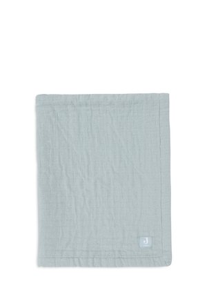 Couverture en coton bleu clair avec une surface texturée, présentant un motif subtil et une petite étiquette de marque dans le coin inférieur droit.