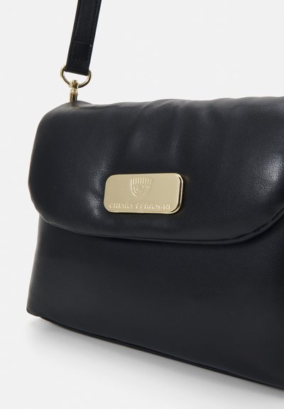 Borsa a tracolla in pelle nera con logo rettangolare dorato e tracolla, primo piano che mostra la texture e i dettagli del marchio.