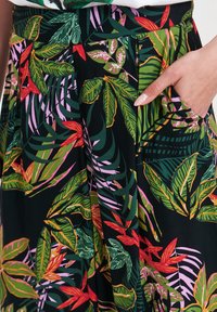 Spódnica w kwiatowy wzór, z czarnym tłem i intensywnymi zielonymi, czerwonymi oraz różowymi liśćmi. Posiada boczne kieszenie dla większej funkcjonalności.