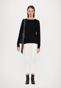 Musta neule, valkoiset slim-fit farkut, mustat nilkkurit hopeisilla yksityiskohdilla ja musta laukku, jossa on rei'itetty olkahihna. Minimalistinen muotoilu.
