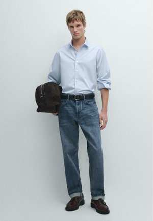 Camicia azzurro chiaro con bottoni, jeans blu scuro, scarpe di pelle marrone e borsa in camoscio marrone scuro. Tessuto liscio, vestibilità casual, colori neutri.