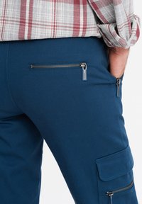 Pantaloni cargo blu con tasca con zip e tasca laterale a pattina, realizzati in un tessuto liscio e con una vestibilità aderente.