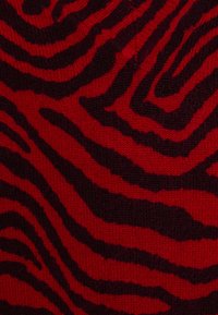 Tissu tricoté rouge avec un motif de rayures de tigre noires. La texture semble douce et légèrement duveteuse, avec des lignes ondulées et irrégulières.