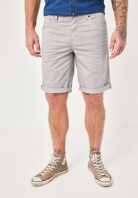 Light gray cotton shorts with rolled cuffs, front pockets, and subtle texture, paired with beige high-top sneakers.