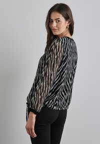Top nero trasparente con un motivo a zig zag in grigio chiaro, maniche arricciate e scollatura rotonda, abbinato a jeans neri aderenti.