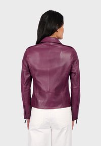 Fialová kožená motocyklová bunda s přiléhavým střihem, ramenními epauletami a zipovými manžetami. Nosit s bílými kalhotami.