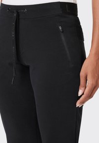 Schwarze Sporthosen mit einem Kordelzugbund, Reißverschlusstaschen und strukturiertem Logodesign, versehen mit einem glatten Stoff und passgenauer Form.