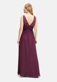 Langes, burgunderfarbenes Abendkleid mit einem Spitzenoberteil, breiten Trägern und einem V-Ausschnitt im Rücken sowie einem flie�ßenden Rock. Mit einem einfachen Gürtel akzentuiert.