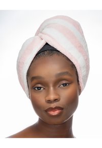 Serviette à rayures blanches et roses, texture douce, design torsadé, portée sur la tête, bande noire en dessous. Le modèle a un maquillage naturel et des lèvres brillantes.