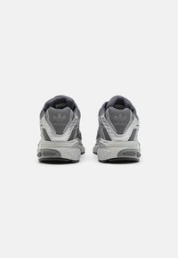 Sive atletske čevlje z teksturiranim mrežastim zgornjim delom, ojačanim petnim delom in masivnim podplatom, vsebujejo izrazite oblazinjenosti in reflektivne detajle.